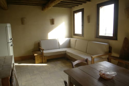 Luminosa zona living del Casale di Poggioferro con sedute rigate, travi in legno e finestre inondate di sole a Poggioferro