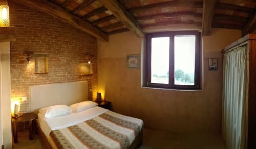 Camera da letto accogliente a Casale di Poggioferro con mattoni a vista, travi di legno e vista sulla campagna dalle ampie finestre