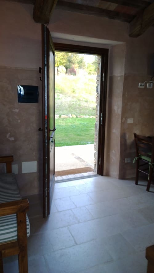 Porta in vetro aperta che rivela l'orto verdeggiante di Casale di Poggioferro in Toscana