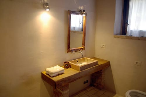 Bagno rustico di Casale di Poggioferro con lavabo in legno, specchio e illuminazione calda nell'appartamento toscano