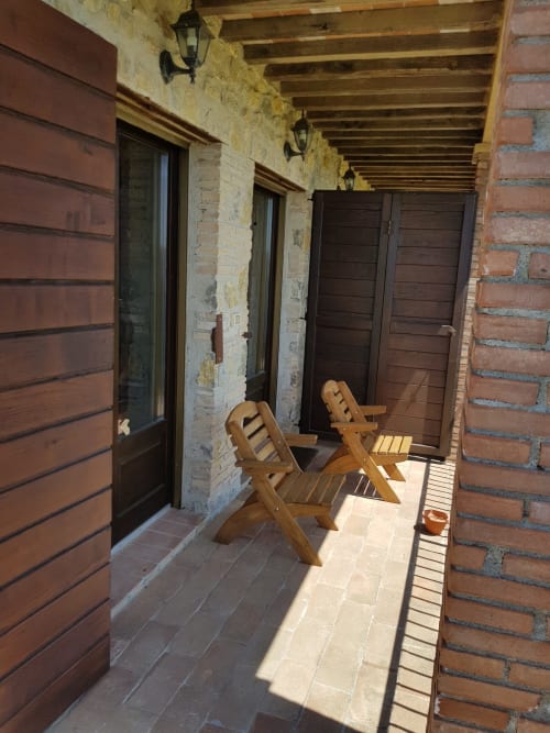 Veranda coperta di Casale di Poggioferro con sedie in legno, muri in pietra e travi a vista in Toscana