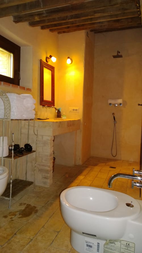 Bagno rustico a Casale di Poggioferro con pareti gialle, travi in legno, lavabo in pietra e doccia moderna.