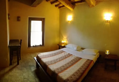 Accogliente camera da letto al Casale di Poggioferro con muri gialli, travi in legno e arredi toscani tradizionali