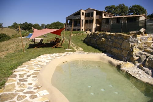 Piscina termale di Casale di Poggioferro con terrazza in pietra, vela ombreggiante rossa e rustica villa toscana in campagna