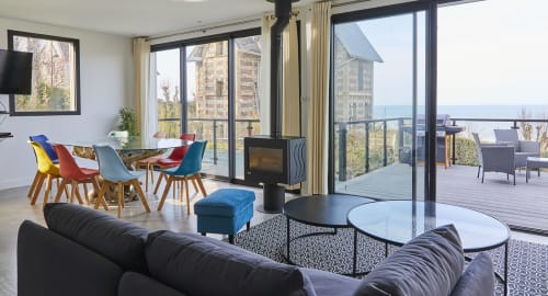 Salle de séjour contemporaine avec de larges baies vitrées donnant sur un panorama côtier exceptionnel.