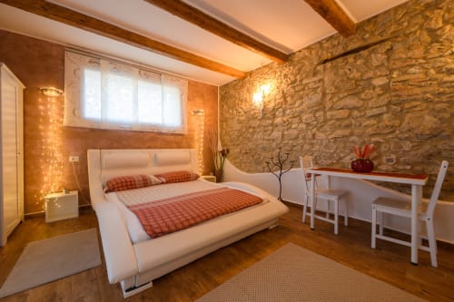 Camera da letto accogliente a Il Podere Prato con muri in pietra, letto bianco, travi in legno e illuminazione calda