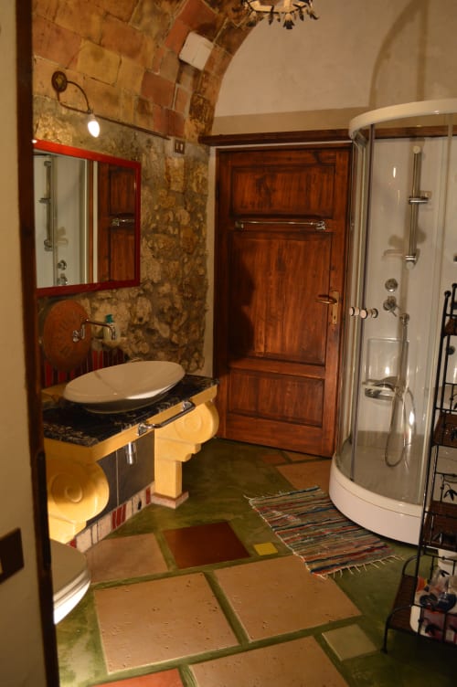 Rustikales Badezimmer in Agri-Bio Santa Palmira in Pomarance mit Keramikwaschbecken, Holztür, runder Dusche und farbigem Fliesenboden.