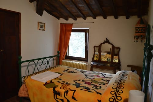 Rustikales Schlafzimmer im Agri-Bio Santa Palmira in Pomarance mit Holzbalken, verziertem Spiegel und farbenfroher ethnischer Bettwäsche