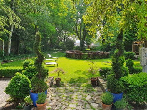 Cour de jardin paisible du gîte Le Grand Duc à Valenciennes avec haies taillées, transats et pelouse luxuriante
