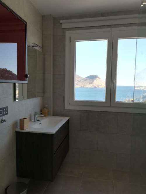 Baño moderno de El Faro De Los Genoveses con vistas al mar Mediterráneo azul y montañas a través de grandes ventanales