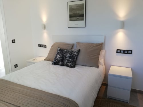 Dormitorio moderno en El Faro De Los Genoveses con cama queen, cabecero gris, mesitas, apliques de pared y vista al mar enmarcada