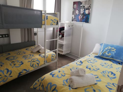 Habitación compartida en El Faro De Los Genoveses en Almería con cama litera, cama individual, ropa de cama floral amarilla y vistas al mar