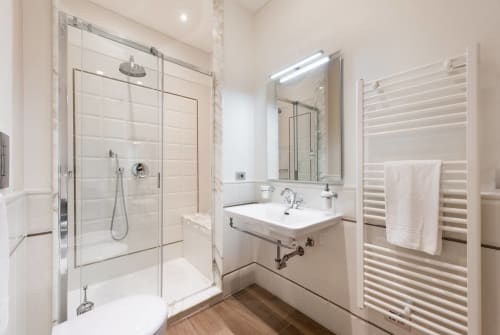Bagno moderno nell'appartamento di Firenze con doccia in vetro, lavabo bianco, scaldarancia e pavimento in legno