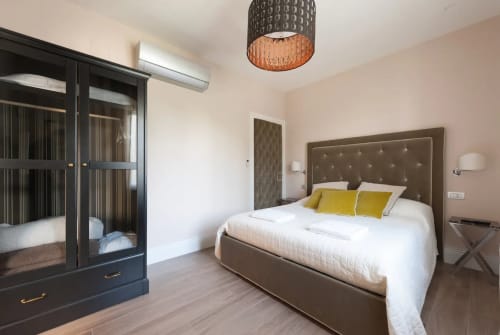 Camera da letto moderna nell'appartamento di Firenze con letto imbottito tortora, cuscini gialli, armadio nero e vista sulla città