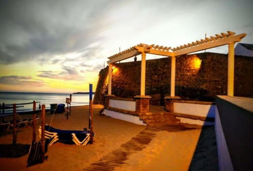 Terraço à beira-mar da Armação Beach Residences ao pôr do sol com pérgula de madeira, espreguiçadeiras e vista para o oceano em Armação de Pêra