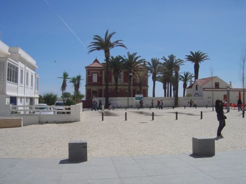 Praça à beira-mar nas Residências de Armação com palmeiras, igreja histórica e largo arenoso em Armação de Pêra, Portugal