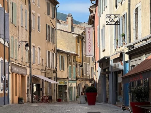 Charming medieval street in Grignan with historic buildings, storefronts, and red planters