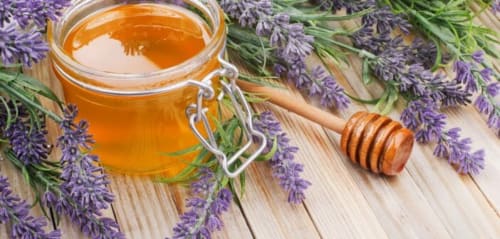 Golden honey in glass jar with wooden dipper surrounded by fresh lavender flowers at Le Pavillon M spa in Grignan