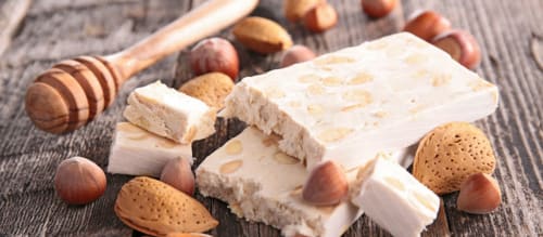 Creamy almond nougat with whole almonds and honey dipper on rustic wood surface at Le Pavillon M