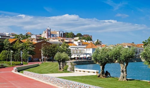 Armação Beach Residences waterfront view with red promenade, olive trees, and historic town with church on hilltop, Portugal