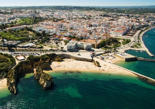 Aerial view of Armação de Pêra beach with golden cliffs, turquoise waters, and whitewashed buildings overlooking the
