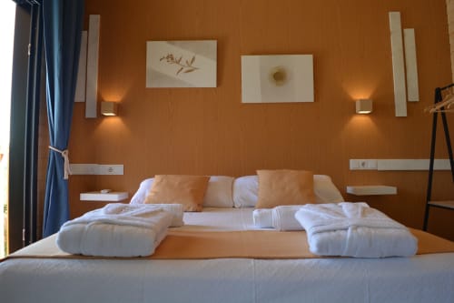 Habitación moderna en Cabañas Compostela con paredes naranja cálido, ropa de cama blanca y arte contemporáneo en Santiago de
