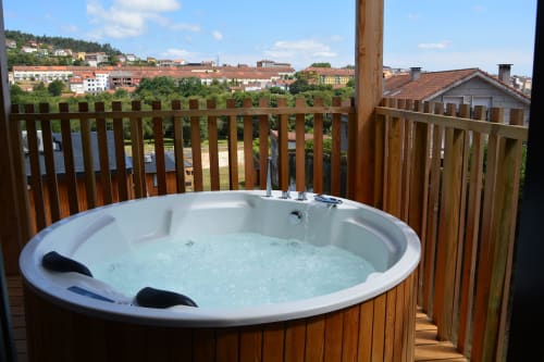 Bañera de hidromasaje al aire libre en terraza de madera con vistas al paisaje urbano de Santiago de Compostela en Cabañas Compostela