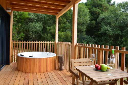 Terraza de madera con jacuzzi y mesa de comedor con vistas al bosque en Cabañas Compostela, Santiago de Compostela