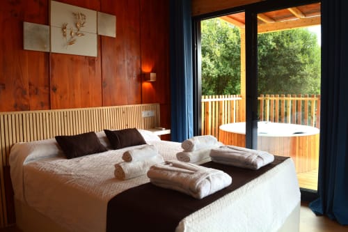 Lujosa habitación en Cabañas Compostela con cama king, cabecero de madera, acceso a terraza y vistas al bosque en Santiago de