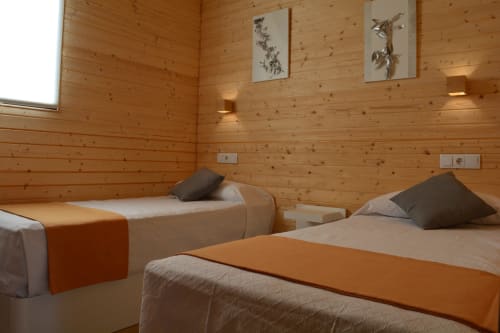 Dormitorio de cabaña moderna en Cabañas Compostela con tres camas, paredes de pino cálido y arte botánico en Santiago de