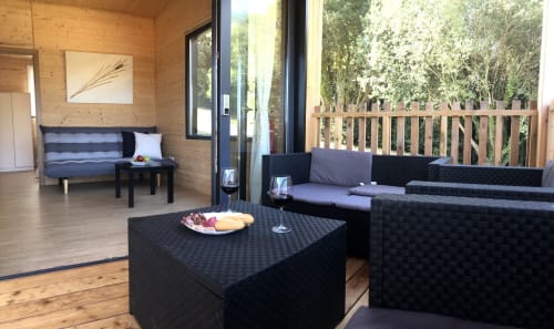 Sala de estar moderna en Cabañas Compostela con muebles de ratán negro, paredes de madera y terraza con vistas al bosque
