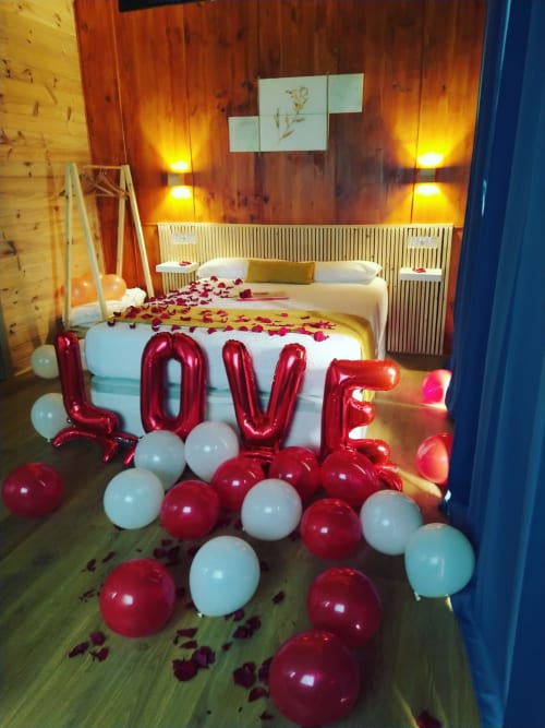 Dormitorio romántico en Cabañas Compostela decorado con globos LOVE, pétalos de rosa e iluminación cálida