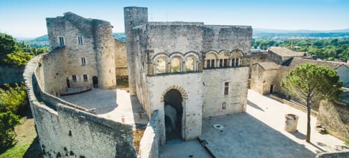 Medieval stone castle courtyard in Grignan, France with towers and arched architecture overlooking green countryside