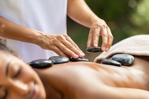Thérapeute appliquant des pierres chaudes lors d'un massage bien-être au centre Le Pavillon M à Grignan