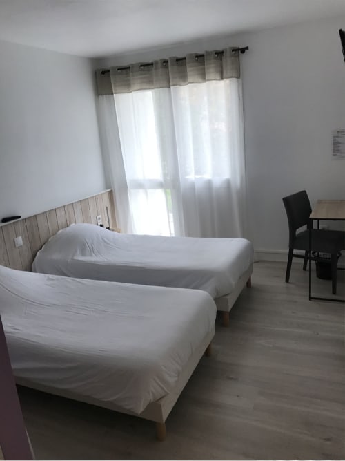 Chambre twin de l'Hôtel De La Bonnheur avec lits blancs, tête de lit en bois et vue sur le jardin à Bracieux