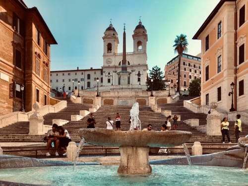 Fontana della Scalinata di Spagna a Roma con chiesa dai due campanili, edifici storici e turisti sulle scale