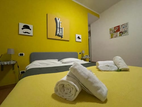Camera da letto gialla luminosa presso l'AD Trastevere Guest House a Roma con asciugamani bianchi arrotolati, letto grigio e arte murale moderna