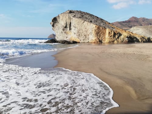 Playa de arena con formaciones rocosas blancas espectaculares y olas en San José, Almería