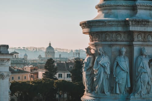 Dettaglio scultoreo neoclassico con veduta dello skyline storico di Roma e cupola sullo sfondo