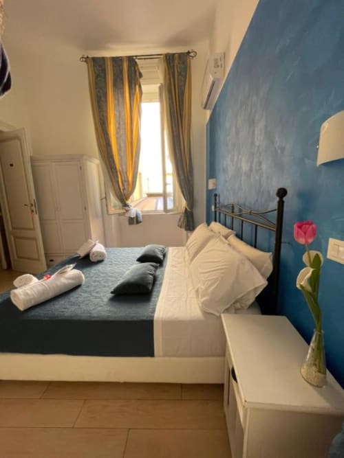 Camera luminosa ad AD Trastevere Guest House con parete blu, letto matrimoniale, tende righe e tulipani rosa fresco.