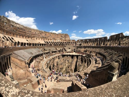 Ancient Roman amphitheater ruins with tiered seating and stone architecture under blue sky, Rome Italy