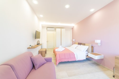 Museo19 deluxe room in Naples with pink accent wall, queen bed, purple sofa, TV, and modern amenities