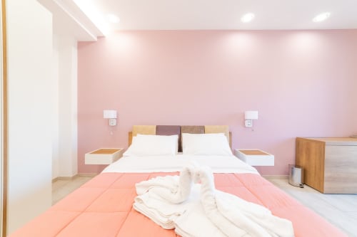 Museo19 Deluxe Room in Naples featuring pink walls, wooden bed frame with white bedding, and modern amenities including TV