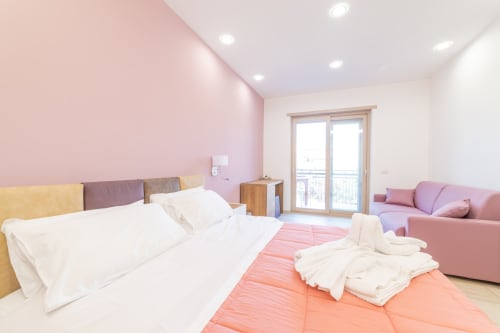 Camera Deluxe al Museo19 Napoli con parete accent rosa, letto matrimoniale, accesso balcone e zona lounge rosa