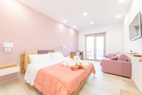 Deluxe Room at Museo19 Naples with pink accent wall, wooden bed, coral bedding, and modern furnishings