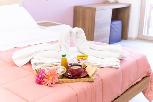 Deluxe Room welcome amenities at Museo19 Naples - fresh towels, breakfast tray with flowers, juice and pastries on pink bed