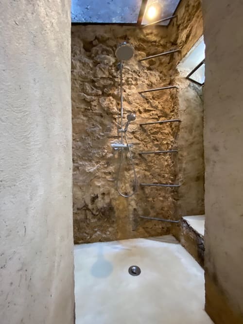 Douche rustique dans un appartement marseillais aux murs de pierre brute, équipements modernes et puits de lumière à Campagne d'Albert