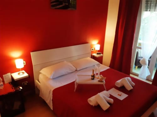 Camera rossa presso AD Trastevere Guest House a Roma con letto bianco, illuminazione calda e vista sulla città dalla finestra