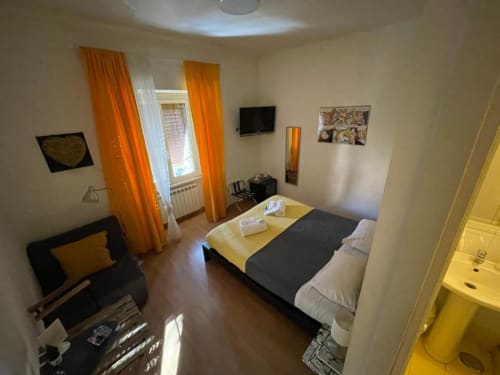 Camera gialla presso AD Trastevere Guest House a Roma con letto, tende arancioni, TV e finestra con vista sulla città
