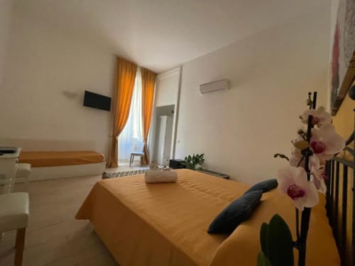 Bright bedroom at AD Trastevere Guest House in Roma with yellow bedding, orchid flower, TV, and window with orange curtains